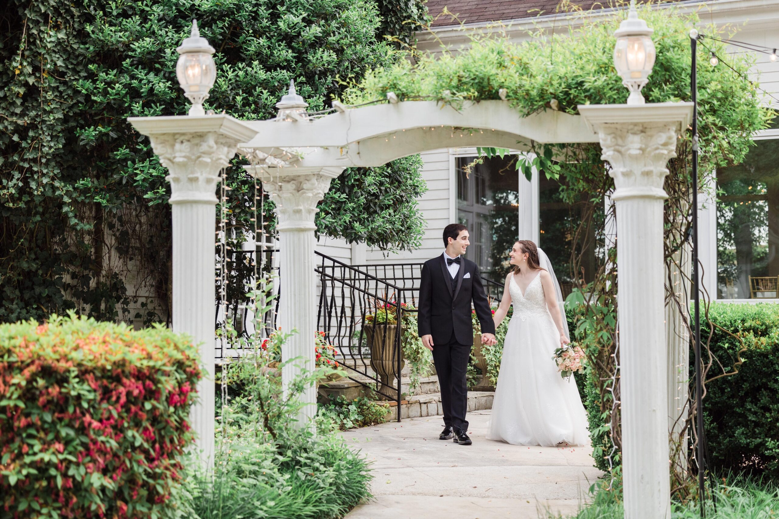 Bride and Groom looking at each other and holding hands while walking towards a white archway
