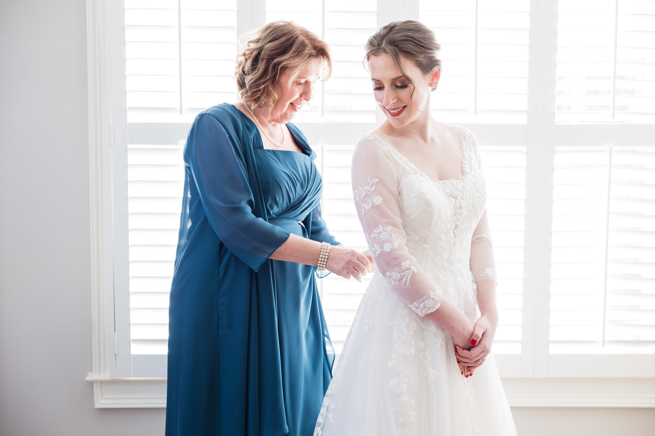 Mother of the bride helping the bride with her dress as she gets ready