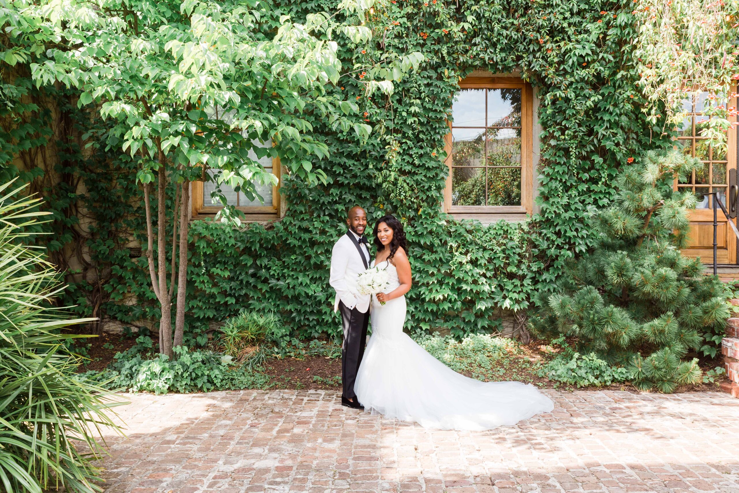 Bride and Groom pose a photo in front of a wall filled with leaves