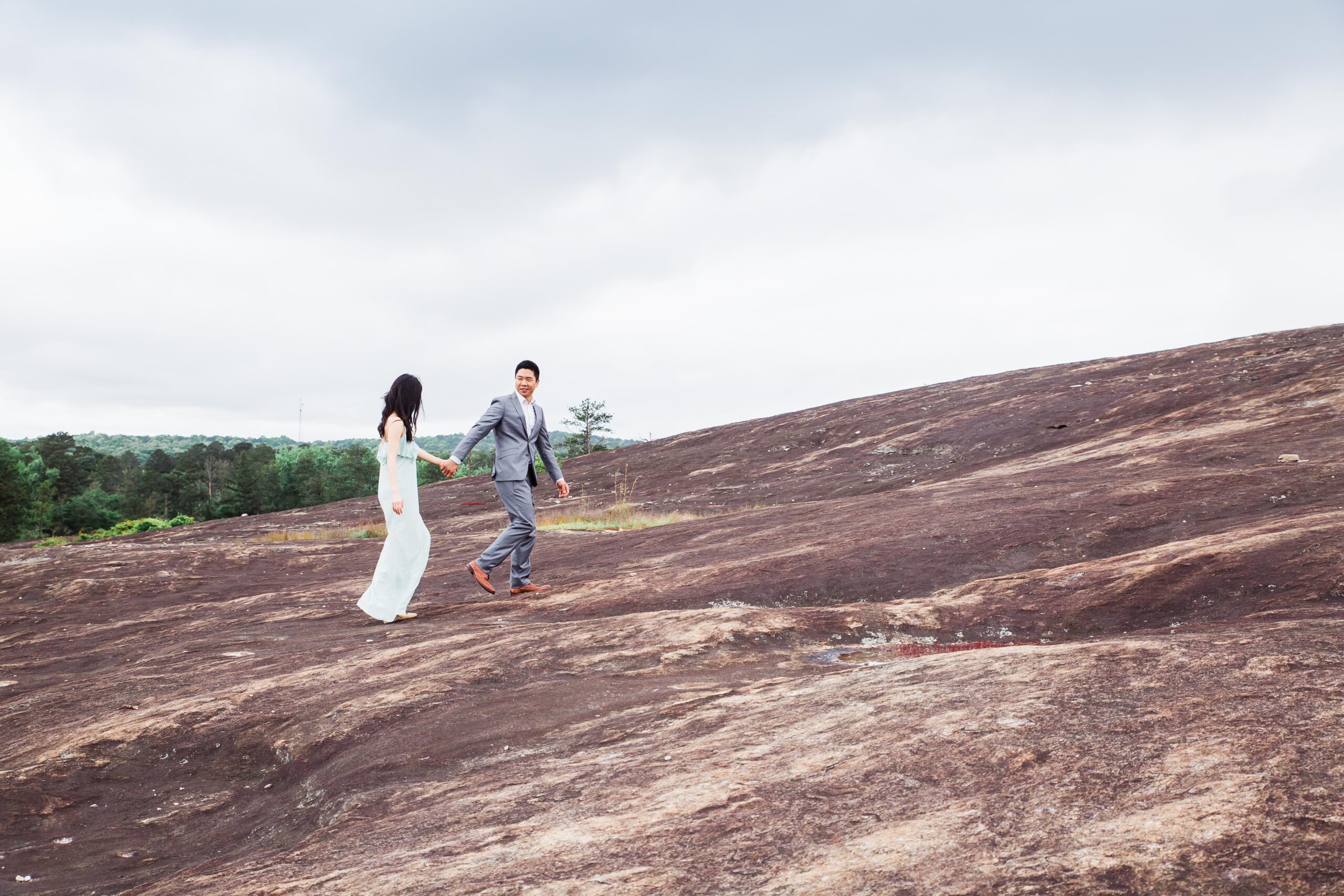groom holding bride's hand as he looks at her while walking up arabia mountain park