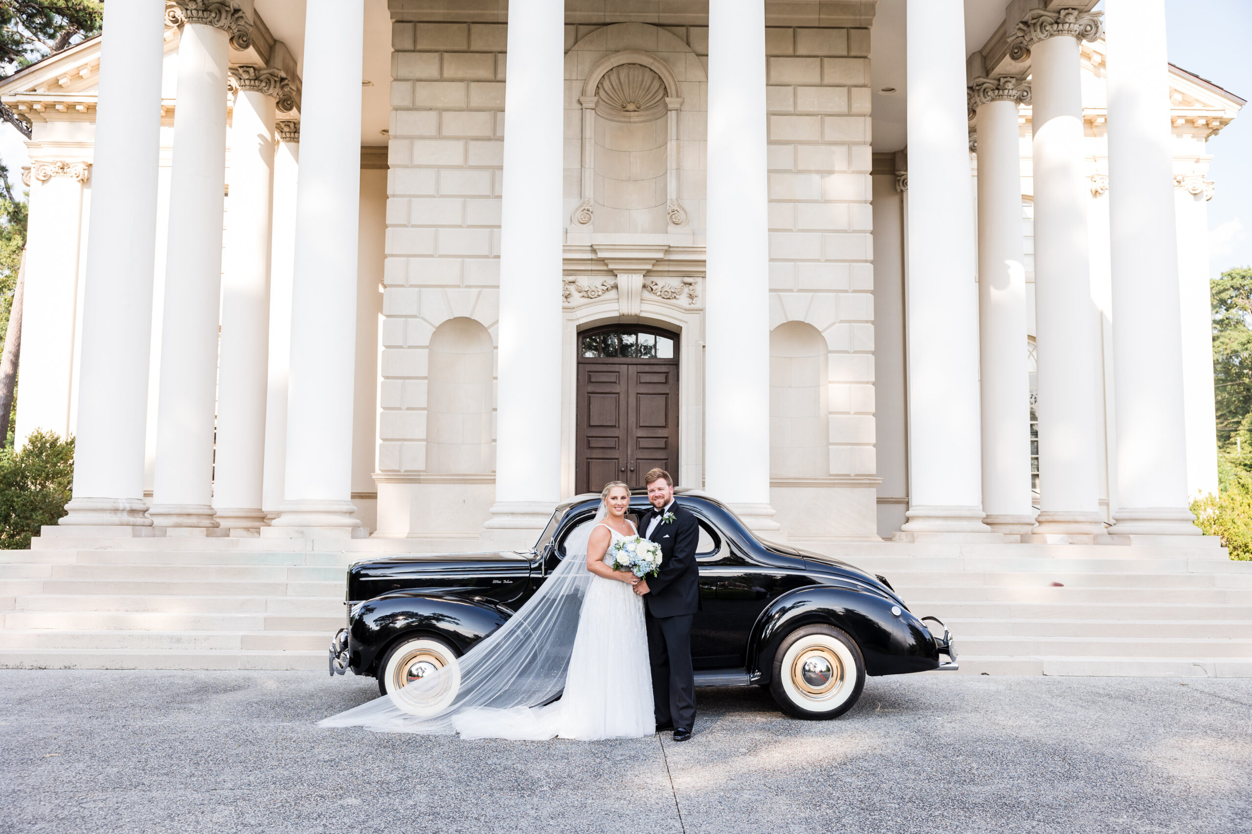 Bride and Groom pose for a photo in front of the vintage bridal car