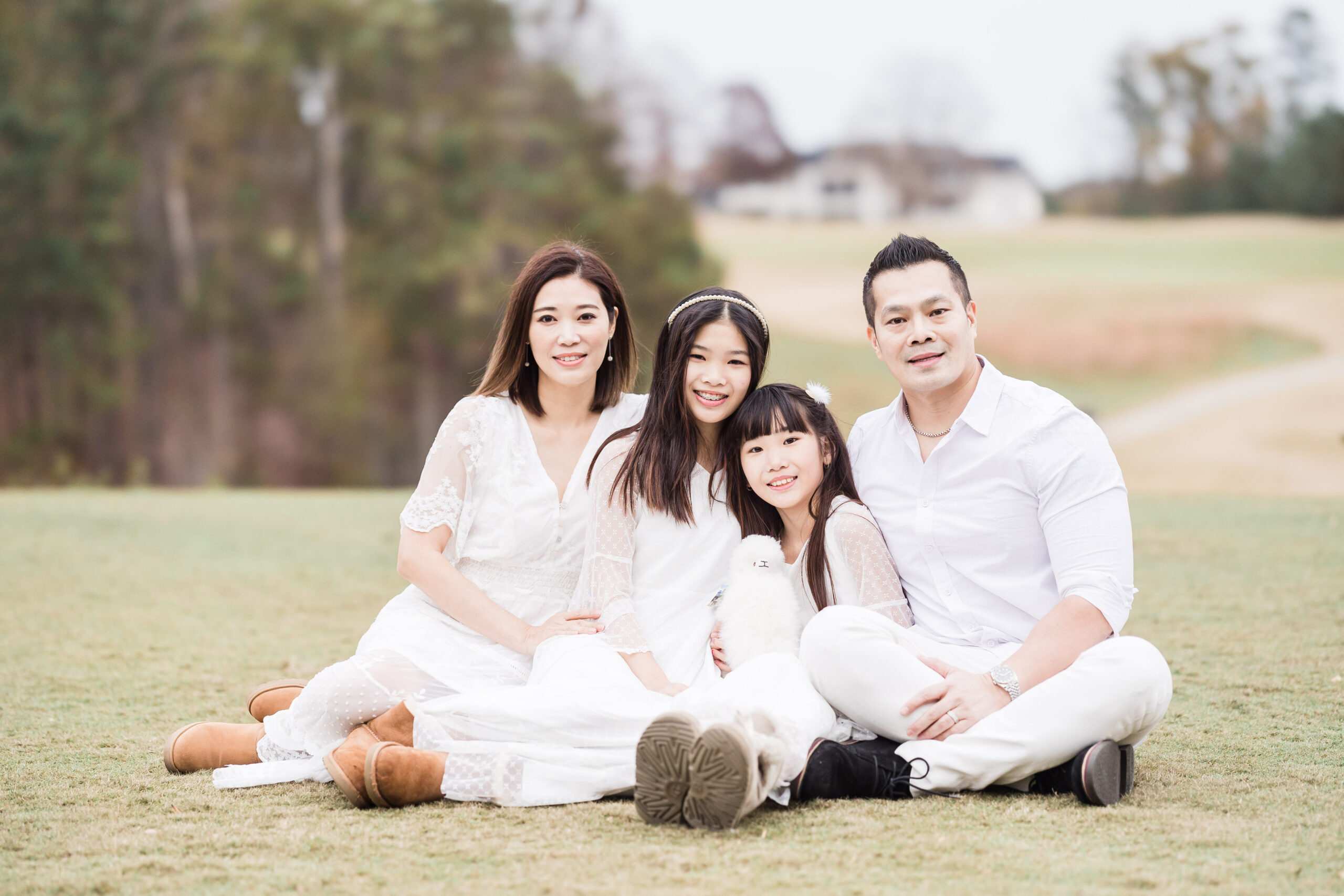 Mom, Dad, and their teo girls in all white sitting in a lawn and smiling at the camera