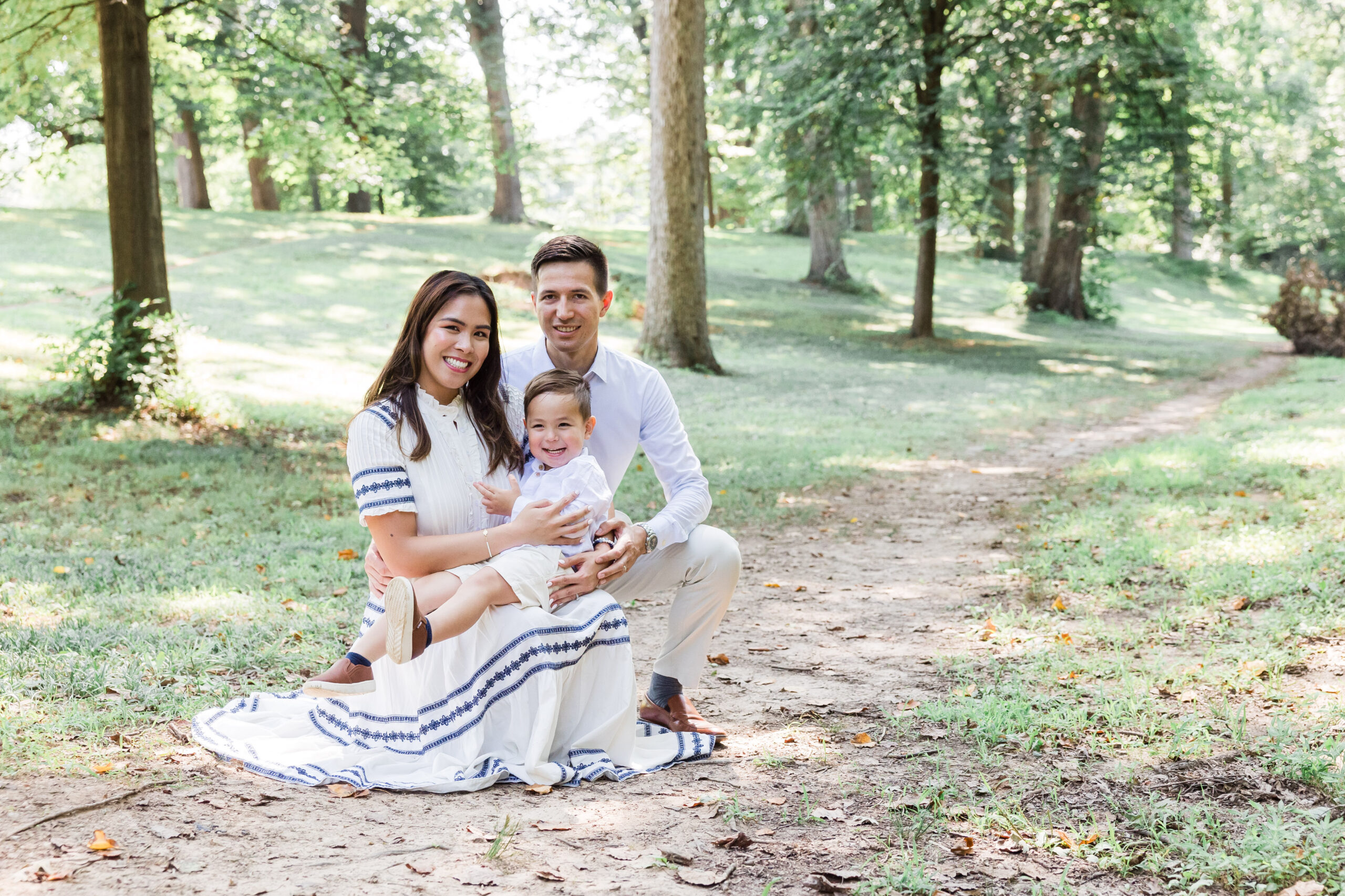 Mom dad and baby sit on the ground surrounding the trees as they pose for the camera