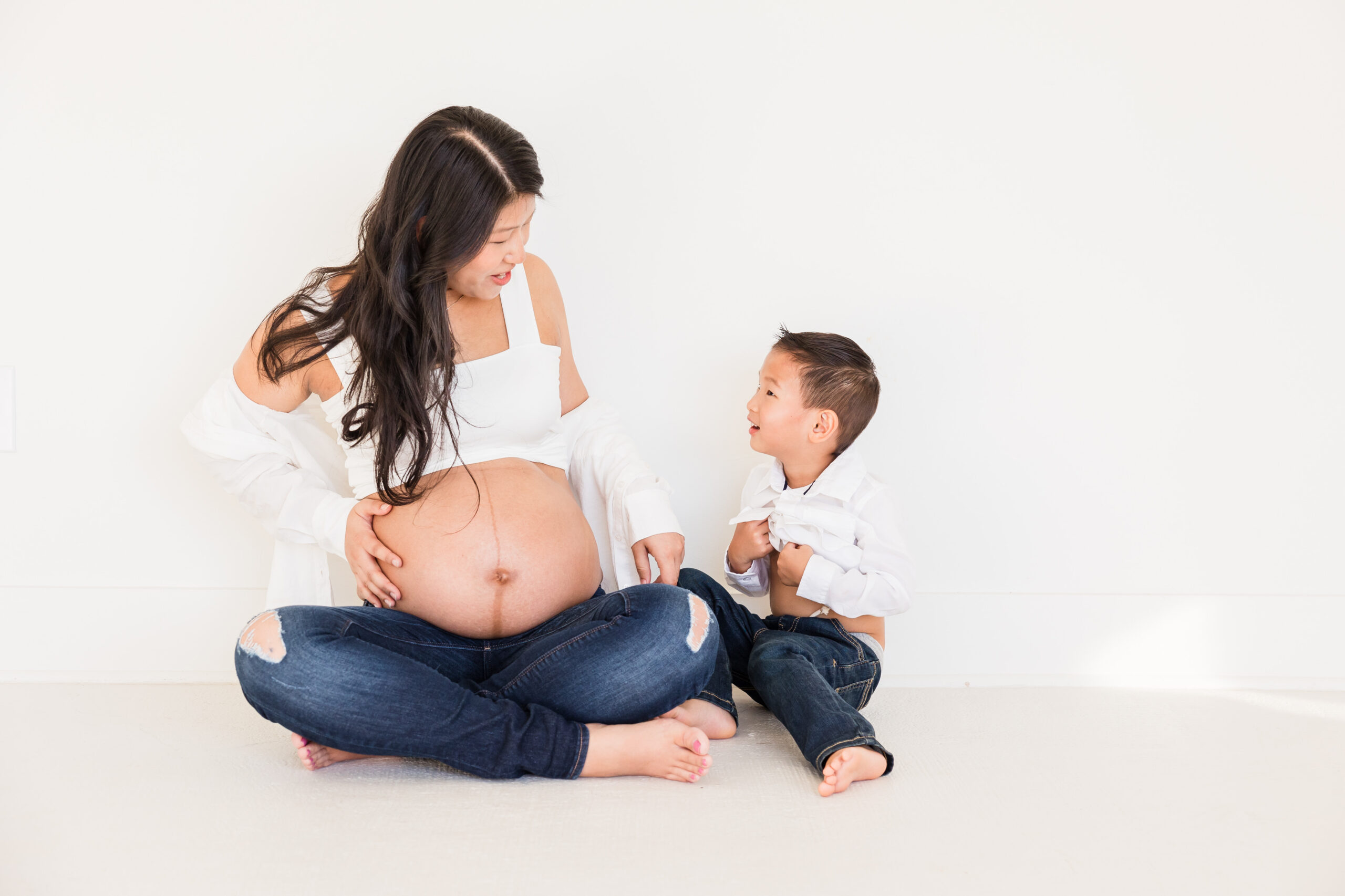 Pregnant mom and son sit on the floor and they look at each other while smiling