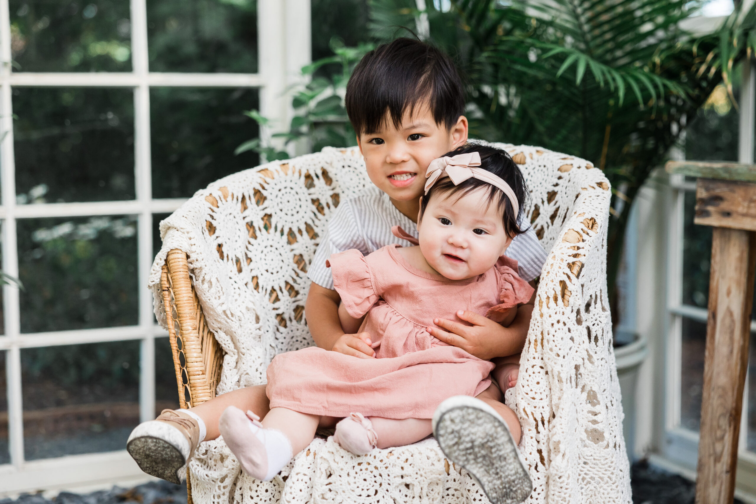 Young boy puts his baby sister on his lap while they smile for the camera