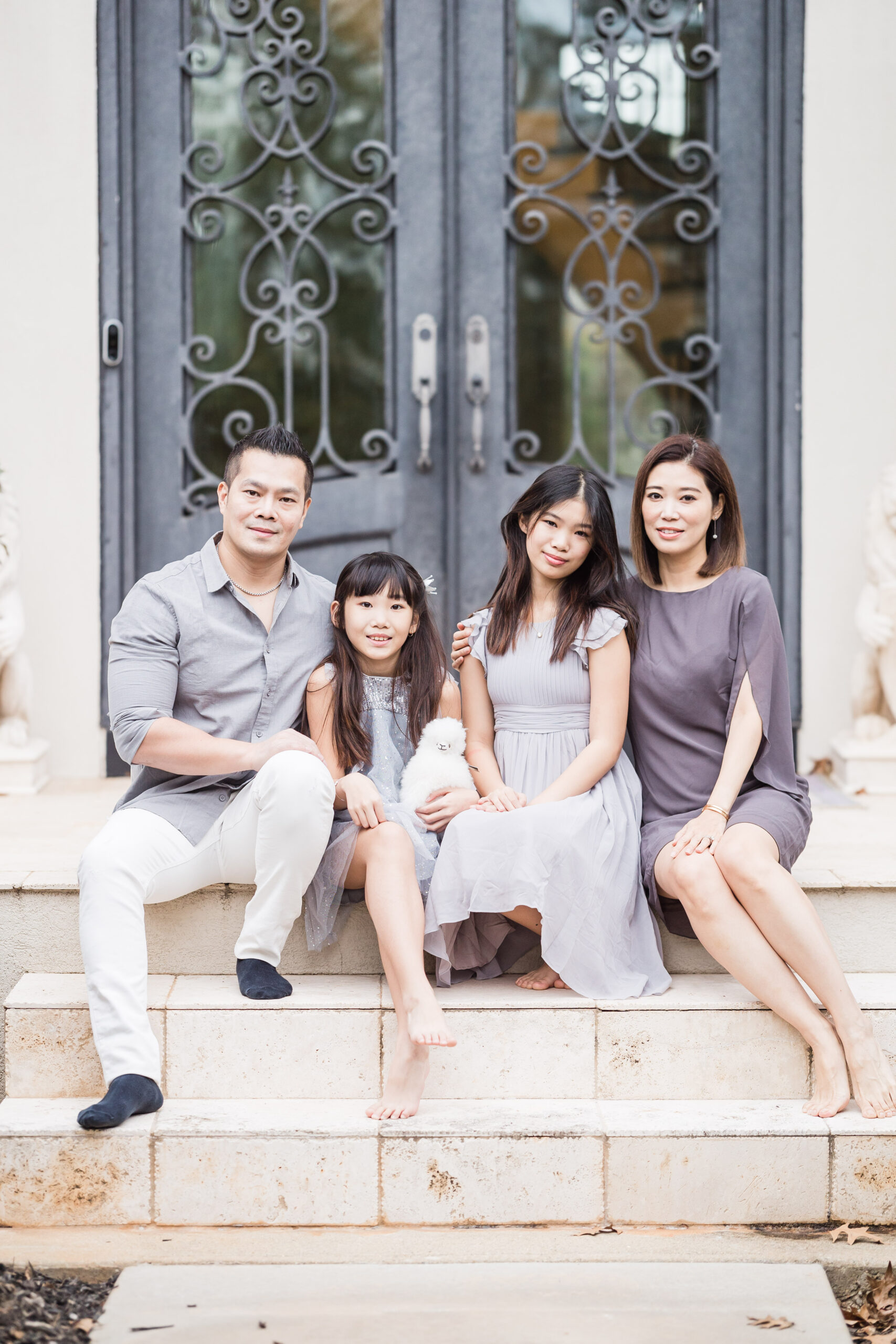 Mom dad and their two daughters sit on their staircase in front of their gray front door