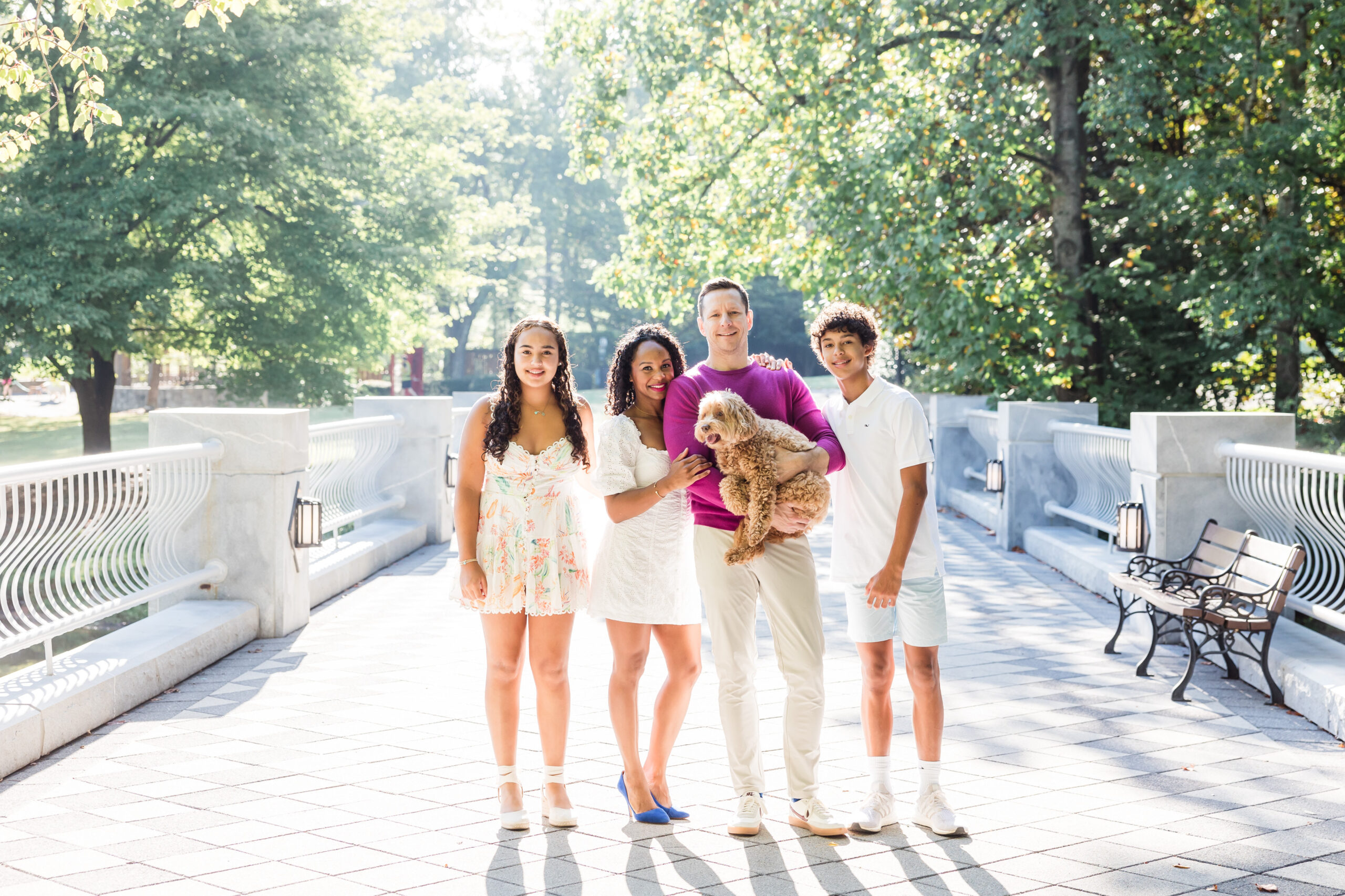 mom, dad, daughter, and son pose for a photo in a park. dad carries their poddle