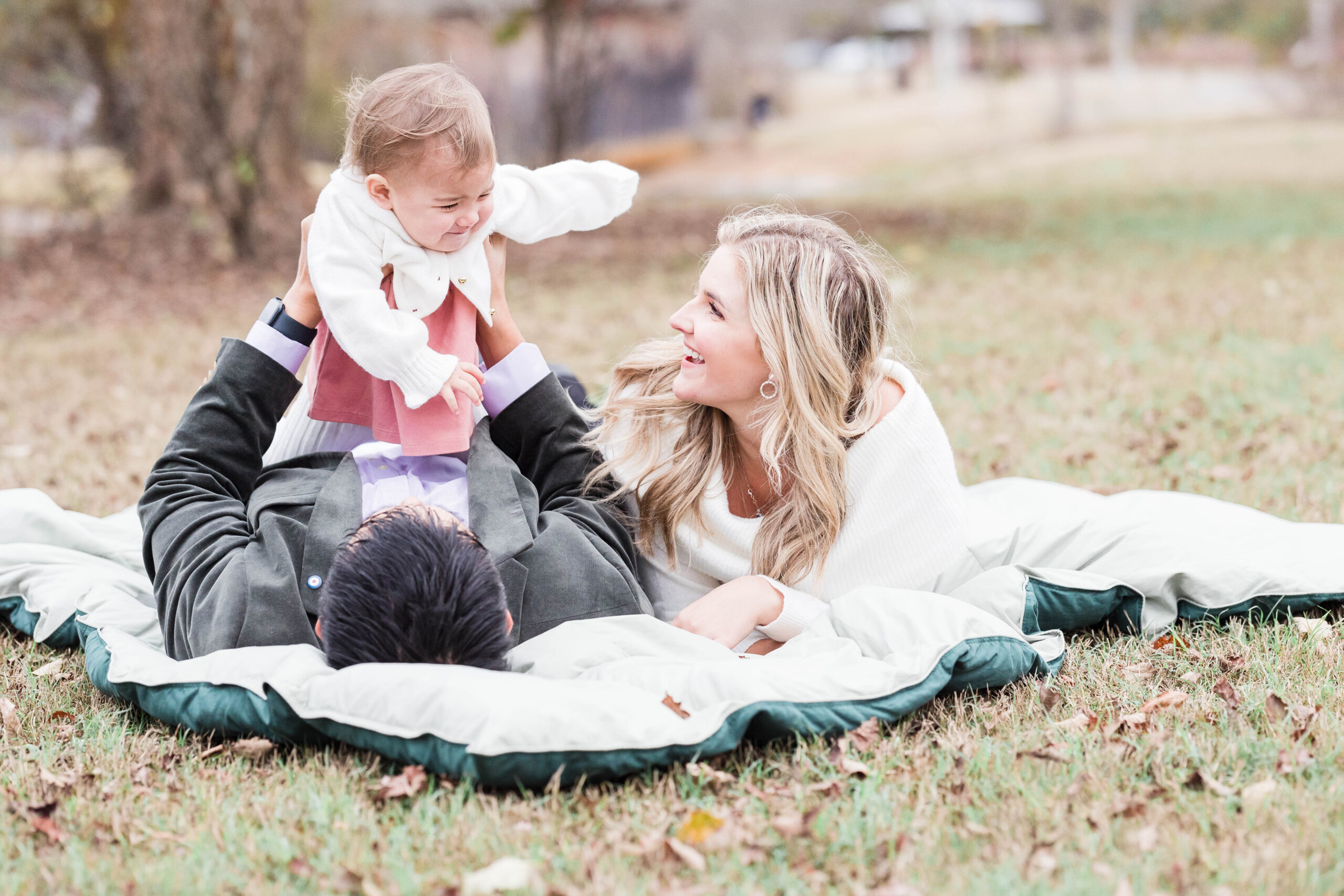 mom, dad, and baby girl lay on a blanket in the park