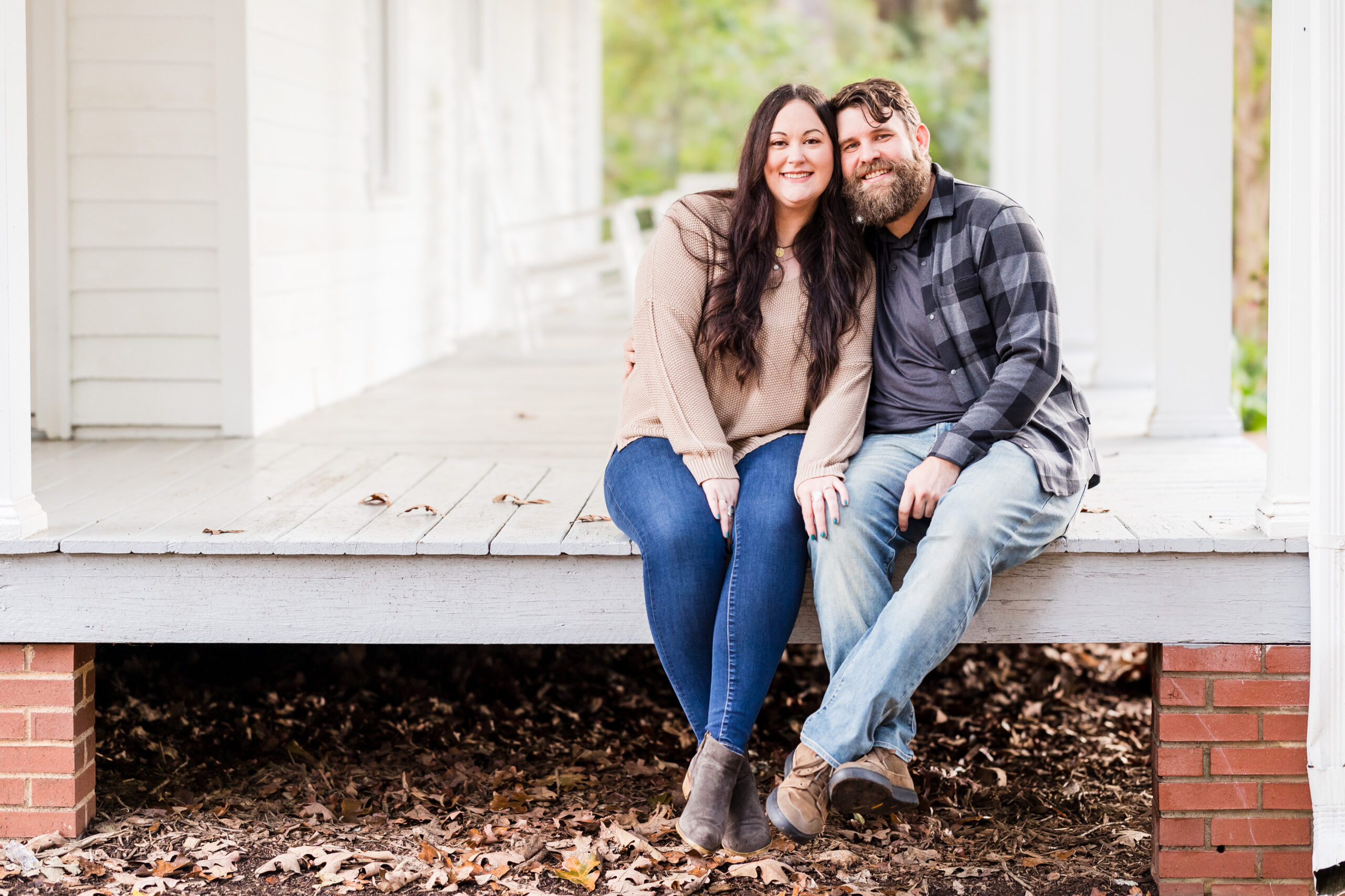 bride and groom sit on the porch as groom put his arm around his bride