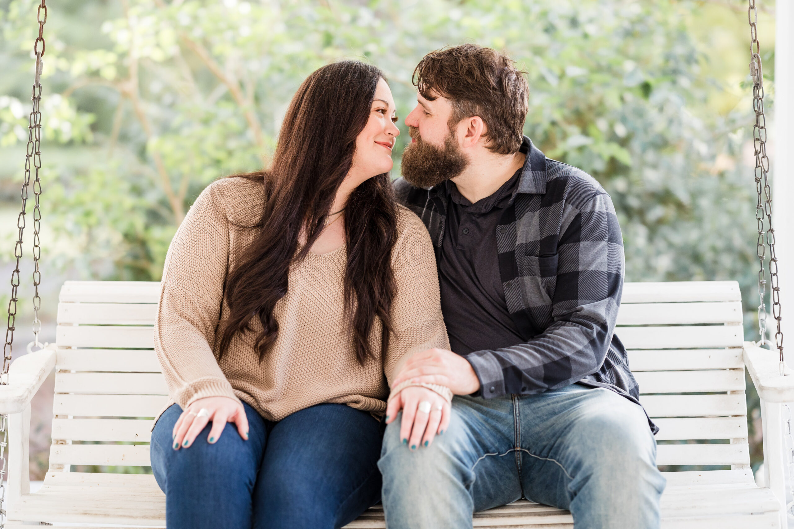 bride and groom sit on a bench as they look at each other while smiling