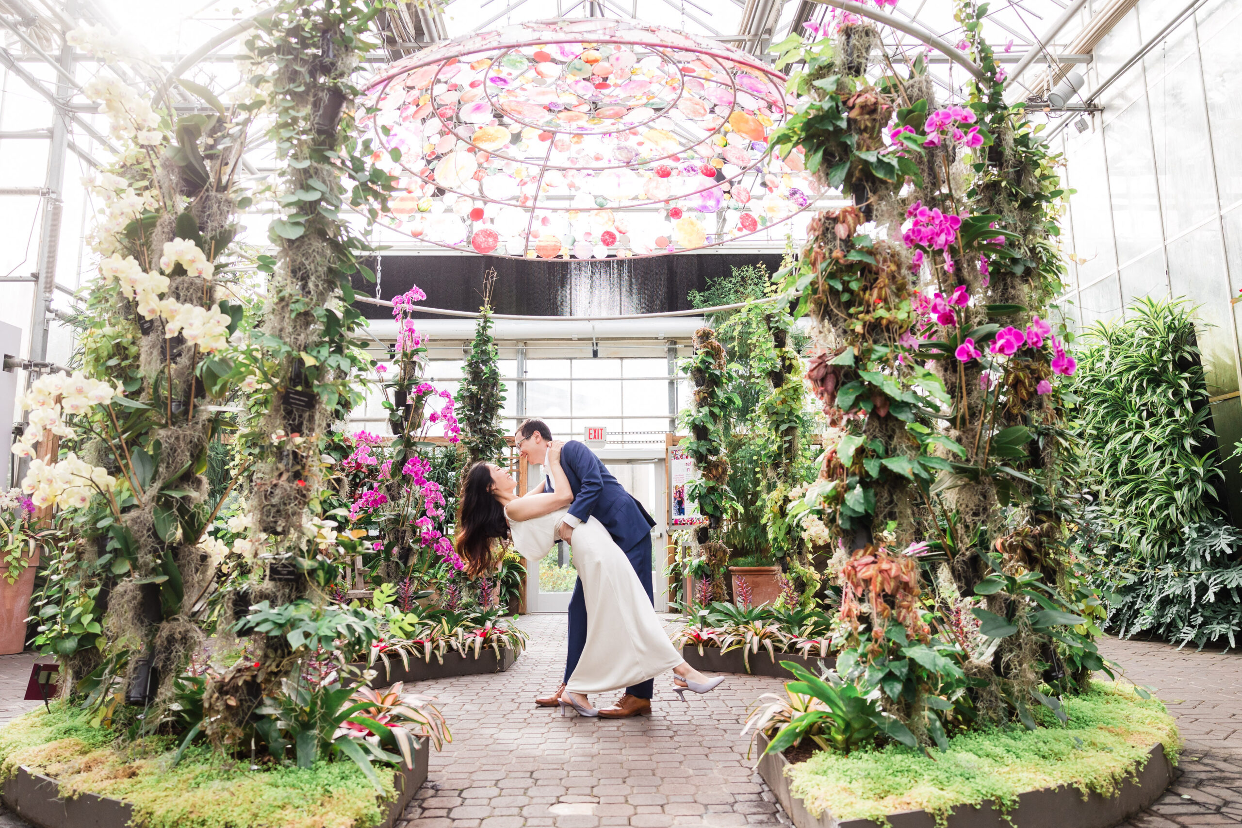 groom dips the bride as they pose in the middle of the greenhouse filled with cascading flowers