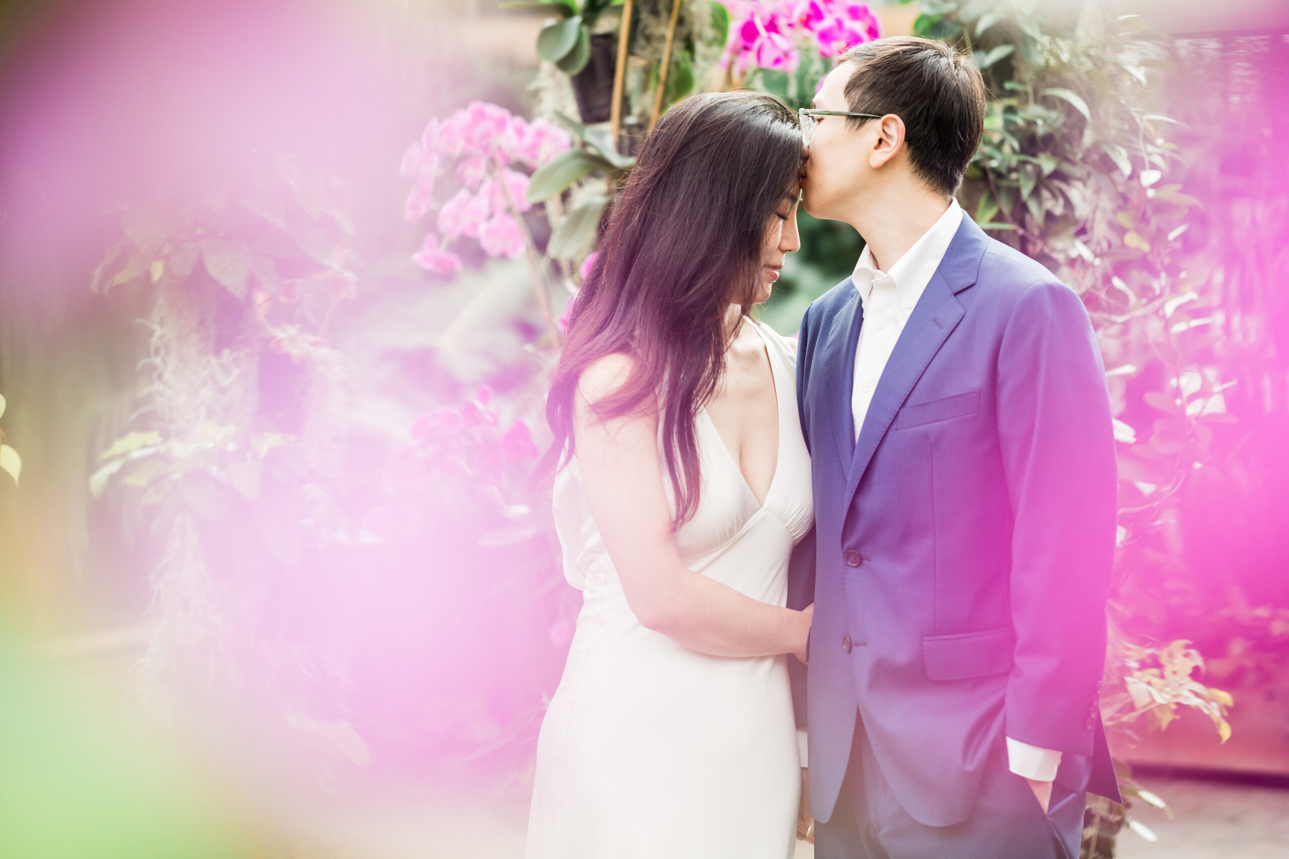 groom gives bride a kiss on the forehead as they pose among the purple orchids